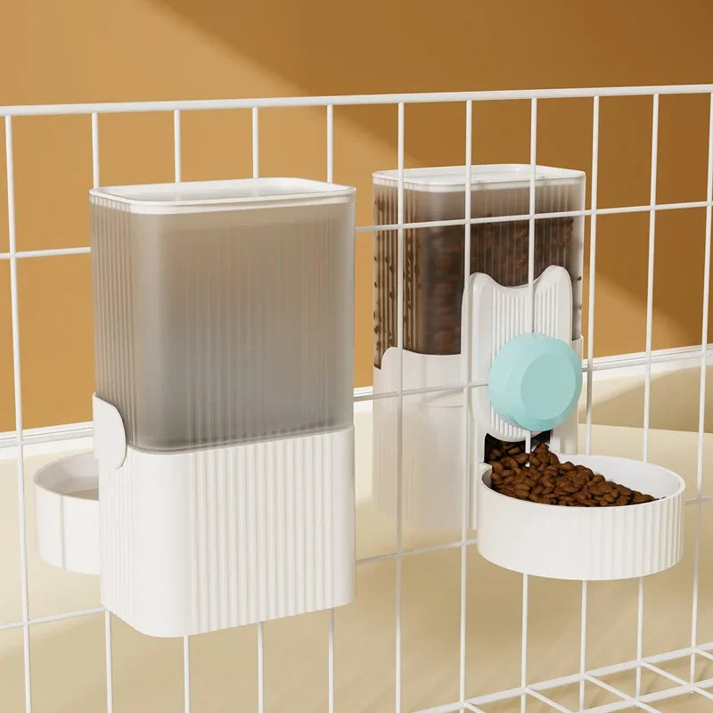  A cat hanging next to a water dispenser, while a dog drinks from a water bowl below. In the background, there is an automatic feeding system, and a rabbit cage with a hanging water bottle. The setup shows various pet supplies for different animals.